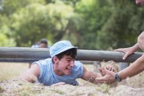 Teammate helping man crawling on boot camp obstacle course — Stock Photo