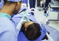 Anestesiólogo con máscara de oxígeno sobre la cara del paciente en quirófano - foto de stock