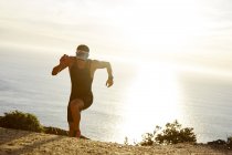 Corredor de triatleta masculino corriendo cuesta arriba en sendero soleado del océano - foto de stock