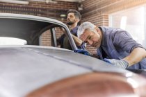 Focused mechanic examining classic car panel in auto repair shop — Stock Photo