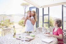 Mother hugging senior mother at patio lunch — Stock Photo