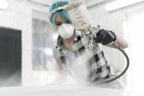 Mujer joven en la máscara protectora aerosol pintura coche en taller de carrocería - foto de stock