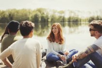 Amigos conversando ao lado do lago ensolarado — Fotografia de Stock