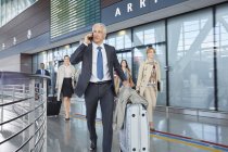 Бізнесмен розмовляє по мобільному телефону, штовхаючи валізу в аеропорту — стокове фото