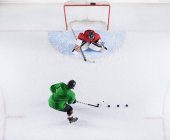 Overhead view hockey player practicing with goalie shooting puck at goal net — Stock Photo