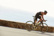 Male triathlete cyclist racing on ocean road — Stock Photo