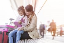 Mother and daughter using digital tablet on bench outside airport — Stock Photo