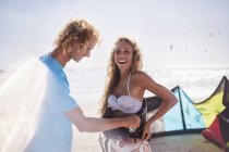 Мужчина пристегивает ремни безопасности к женщине на солнечном пляже — стоковое фото