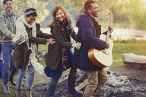 Playful friends with guitar dancing in conga line at campsite — Stock Photo