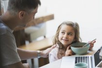Padre e figlia a fare colazione al computer portatile — Foto stock