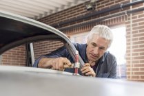 Mechaniker mit Hammer auf Motorhaube in Autowerkstatt — Stockfoto
