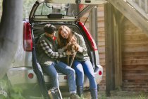 Couple petting dog at back of car outside sunny cabin — Stock Photo