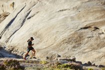 Male triathlete runner running on sunny rocky trail — Stock Photo