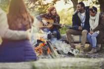 Friends playing guitar and drinking beer at campfire — Stock Photo