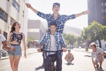 Teenage friends riding BMX bicycle and skateboarding on sunny urban street — Stock Photo