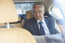Businessman reviewing paperwork in back seat of town car — Stock Photo