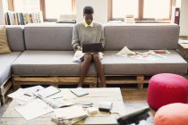 Творческая предпринимательница печатает на цифровом планшете на диване в офисе — стоковое фото