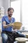 Homem maduro segurando tigela na roda de cerâmica no estúdio — Fotografia de Stock
