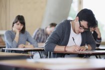 Estudiante universitario masculino enfocado tomando prueba en el escritorio en el aula - foto de stock