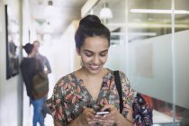 Sorrindo estudante universitário feminino mensagens de texto no corredor — Fotografia de Stock