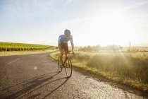 Male triathlete cyclist cycling on sunny rural road at sunrise — Stock Photo