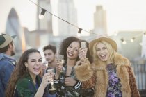 Retrato entusiastas mujeres jóvenes bebiendo champán en la fiesta en la azotea - foto de stock
