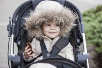 Smiling girl in fur hood riding in stroller — Stock Photo