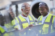 Trabajadores de la tripulación de tierra de control de tráfico aéreo hablando con tableta digital en asfalto del aeropuerto - foto de stock