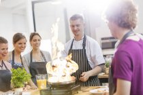 Students watching teacher flambe in cooking class kitchen — Stock Photo