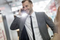 Улыбающийся бизнесмен разговаривает по мобильному телефону в аэропорту — стоковое фото