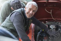Портрет улыбающийся механик фиксирующий двигатель в авторемонтной мастерской — стоковое фото