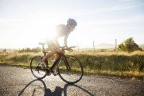 Ciclismo masculino de triatleta en carretera rural soleada al amanecer - foto de stock