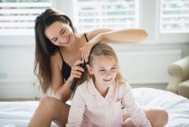 Madre spazzolando i capelli della figlia sul letto — Foto stock