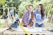 Portrait of smiling volunteers with digital tablet and blueprints at construction site — Stock Photo
