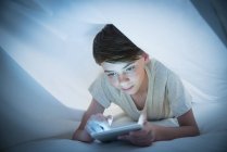 Мальчик с цифровым планшетом под листом — стоковое фото