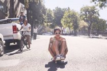 Дівчина-підліток сидить на скейтборді на сонячній міській вулиці — стокове фото