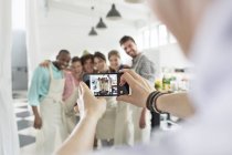 Мужчина фотографирует студентов кулинарного класса на кухне — стоковое фото
