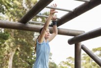 Determined woman crossing monkey bars on boot camp obstacle course — Stock Photo