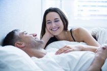 Улыбающаяся пара, лежащая в постели и разговаривающая вместе — стоковое фото