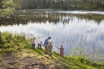 Grand-père enseignant la pêche aux petits-enfants au bord du lac ensoleillé — Photo de stock