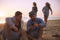 Друзі гуляти текстові повідомлення з мобільного телефону на пляж заходу сонця — стокове фото