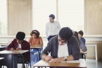 Professor assistindo estudantes universitários fazendo teste em sala de aula — Fotografia de Stock