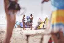 Personas con equipo de kitesurf hablando en la playa soleada - foto de stock