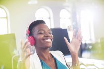 Smiling businesswoman listening to music on headphones in office with eyes closed — Stock Photo