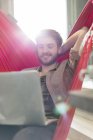 Casual businessman using laptop in hammock in sunny office — Stock Photo