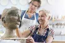 Учитель, направляющий старшую женщину, которая делает глиняное лицо в мастерской керамики — стоковое фото