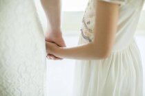 Image recadrée de mariée tenant la main de demoiselle d'honneur dans la chambre domestique — Photo de stock