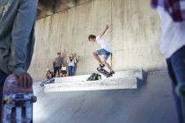 Друзі дивляться і підбадьорюють хлопчика-підлітка скейтбордингу в скейтборді парку — стокове фото