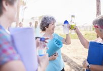 Mujeres mayores brindando botellas de agua después de la clase de yoga en el parque - foto de stock