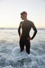 Male triathlete in wet suit standing in ocean surf — Stock Photo